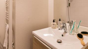 A bathroom with a white sink, a mirror, a shower, and toiletries.