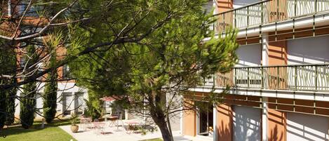 A multi-story building with balconies, a grassy courtyard, and outdoor seating.