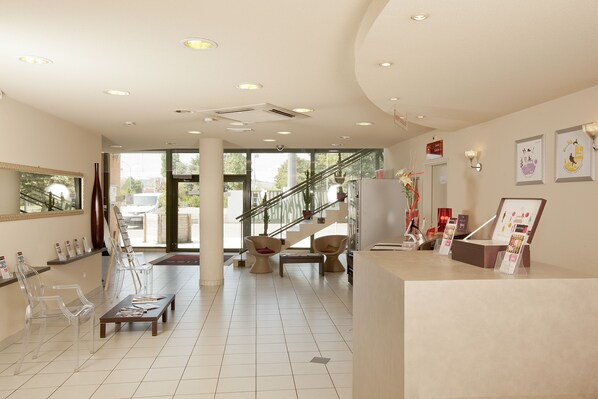 A spacious lobby with clear chairs, a reception desk, and a staircase leading to upper floors.