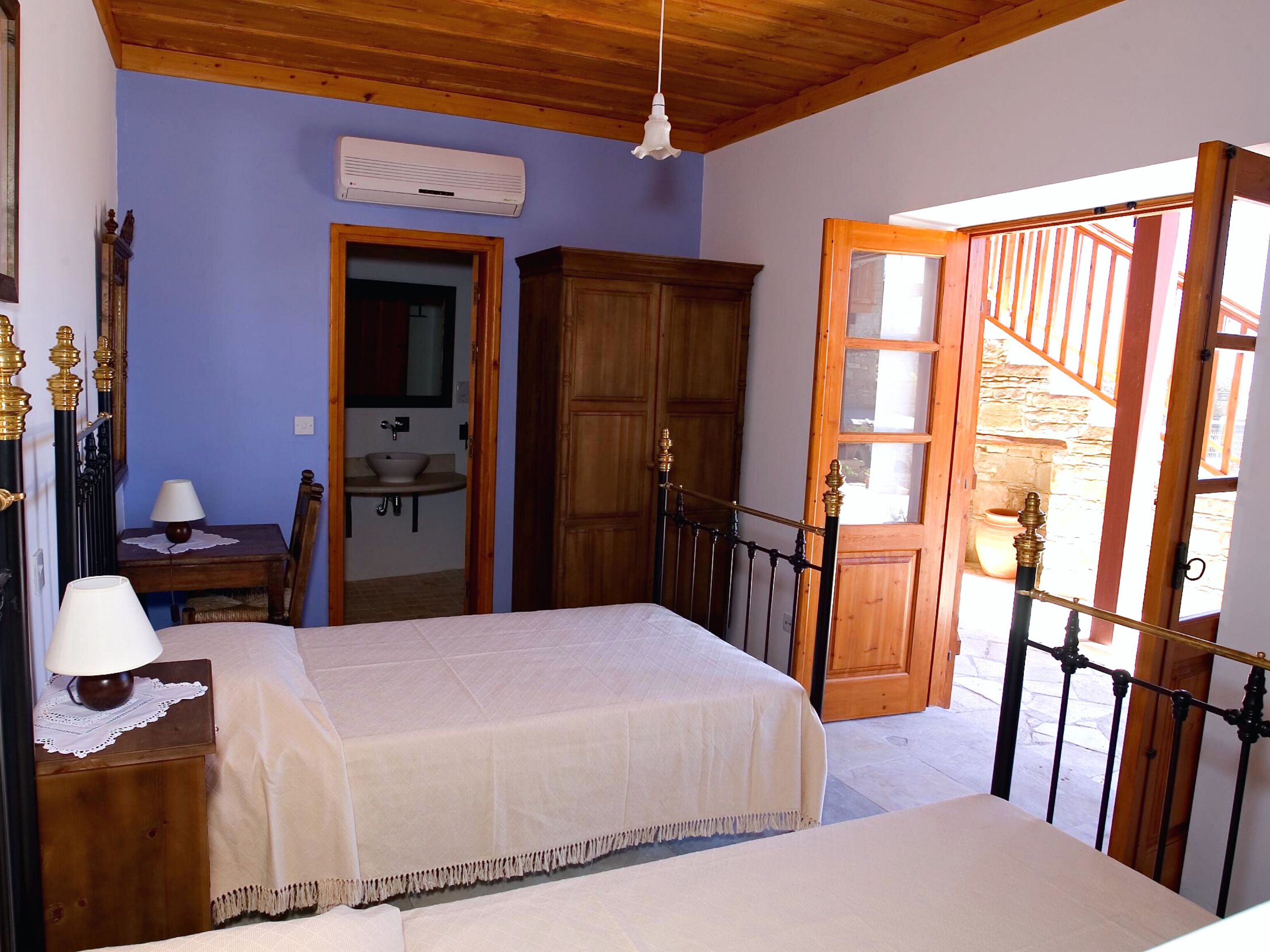 A bedroom with a bed, a wooden wardrobe, a bathroom, and a staircase leading outside.