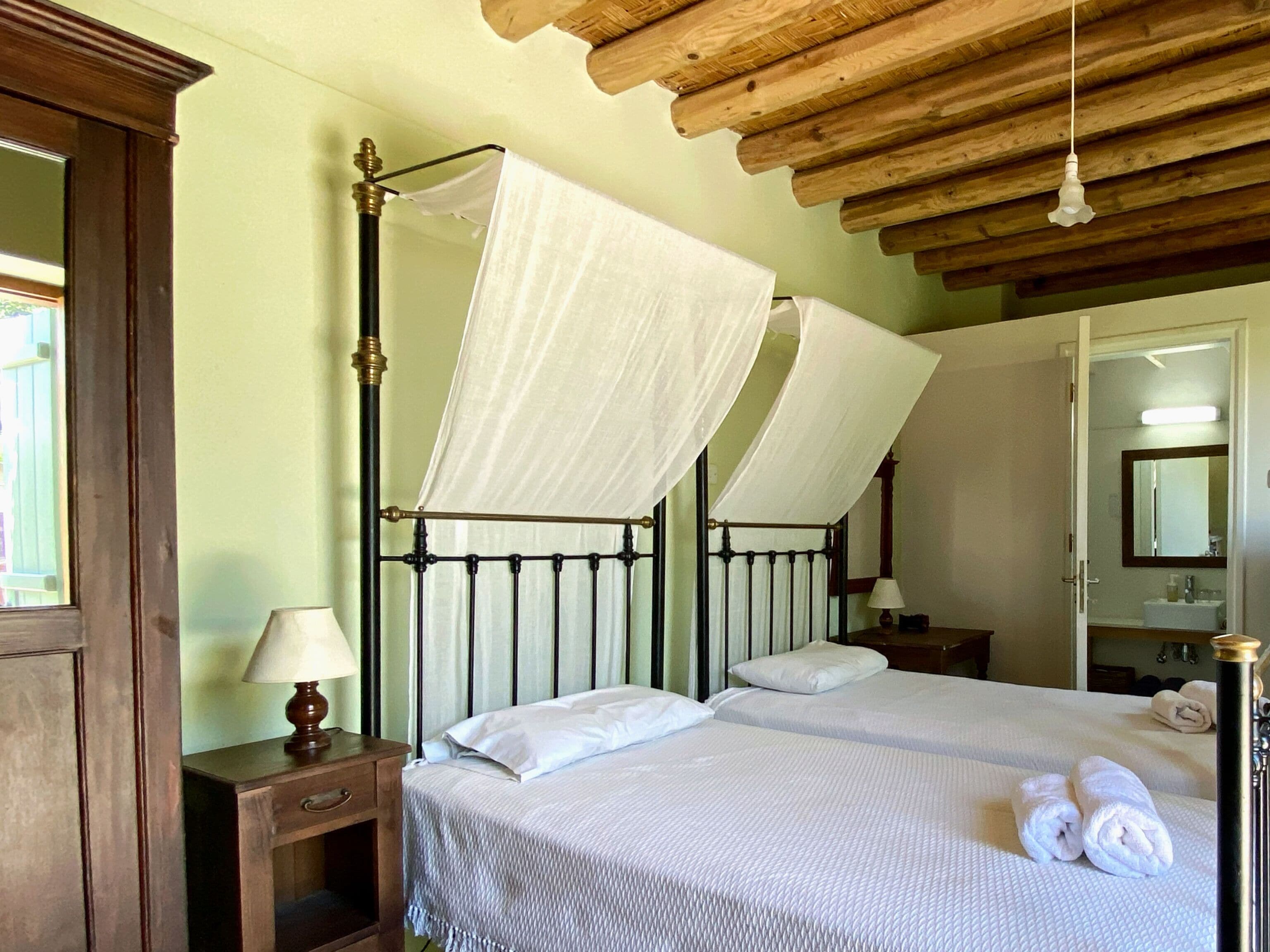 A double bed with a canopy, a bedside table with a lamp, and a wooden ceiling.