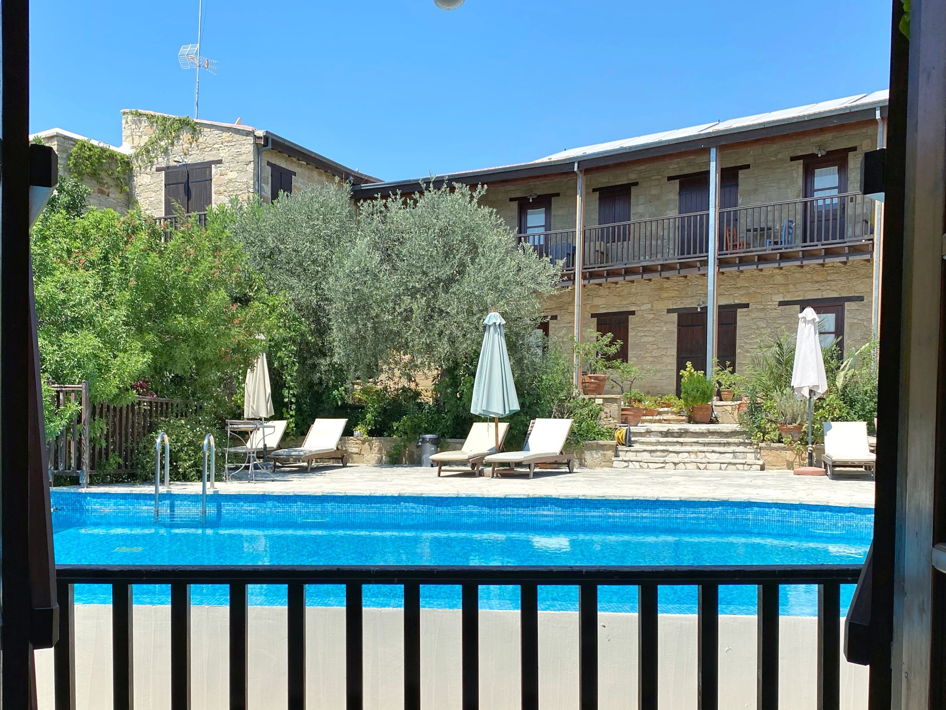 A pool area with lounge chairs and umbrellas, surrounded by stone buildings with balconies.