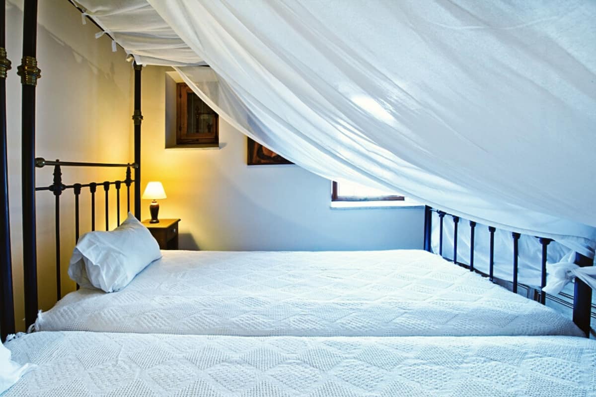 A bedroom with a canopy bed, a bedside table with a lamp, and a window.