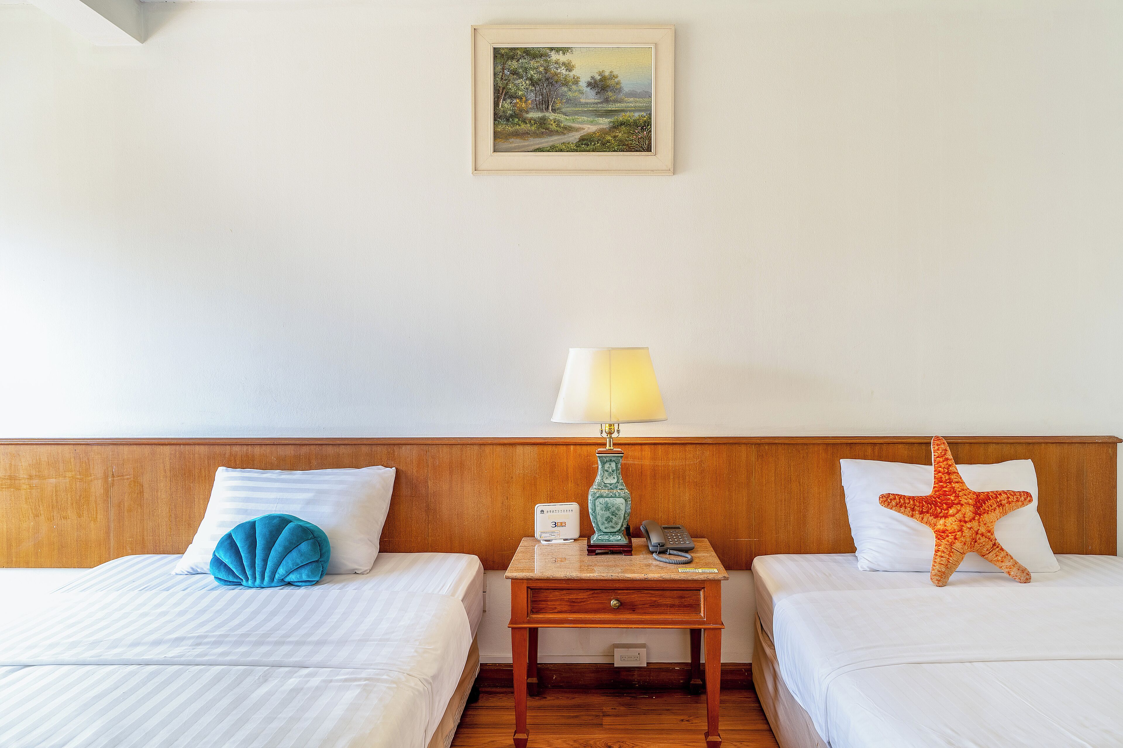 A hotel room with two beds, a nightstand with a lamp, a phone, and a starfish decoration.