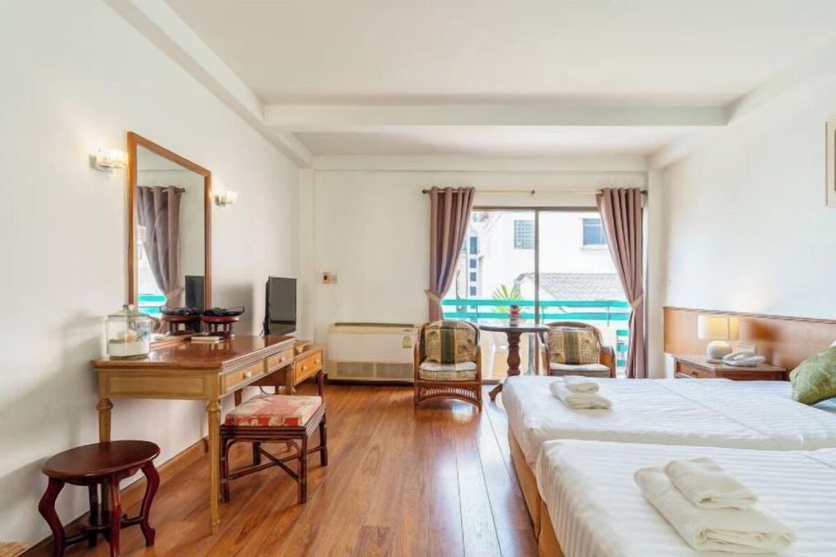 Habitación de hotel con escritorio de madera, dos sillas, una cama con toallas, televisor y ventana con cortinas.