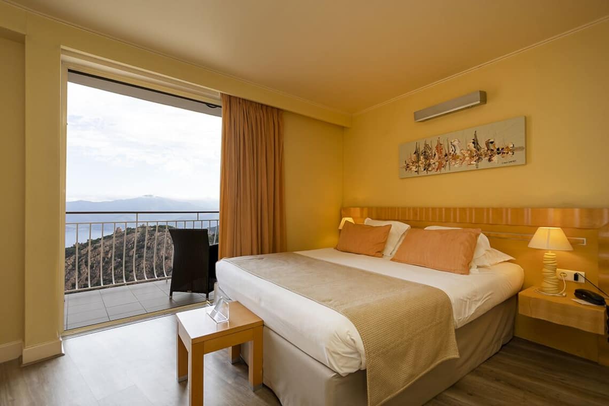 A hotel room with a bed, bedside table, and a view of the mountains.
