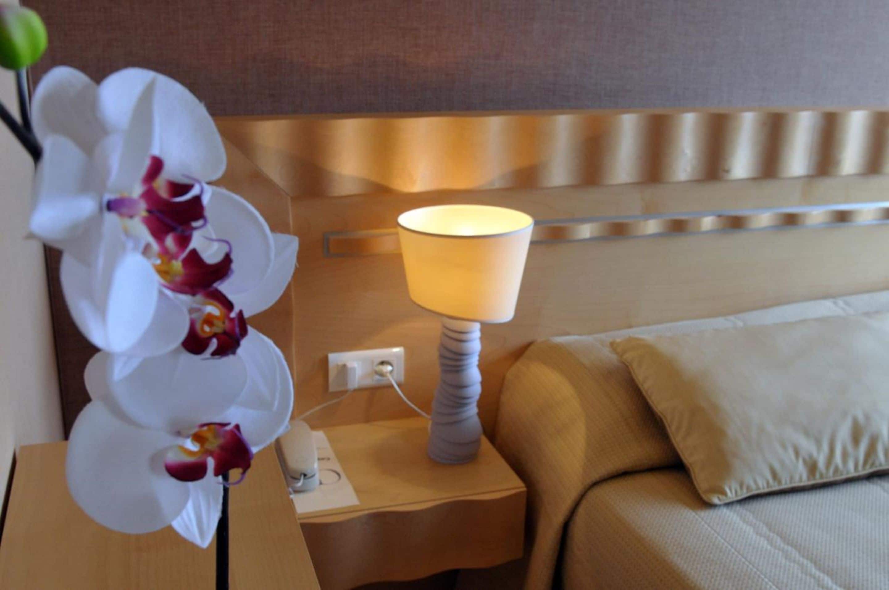 Une chambre d’hôtel avec un lit, une table de chevet avec une lampe et une plante orchidée.