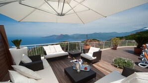 Una terraza con mobiliario exterior, una bandeja de champán y vistas al mar y las montañas.