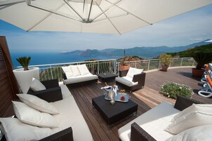 Una terraza con mobiliario exterior, una bandeja de champán y vistas al mar y las montañas.