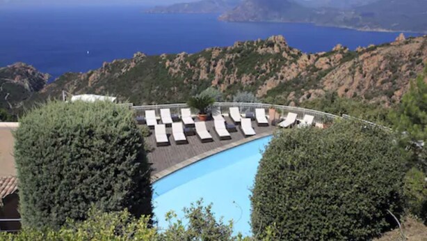 Una piscina con sillas de descanso, rodeada de follaje y con vistas a un paisaje costero.