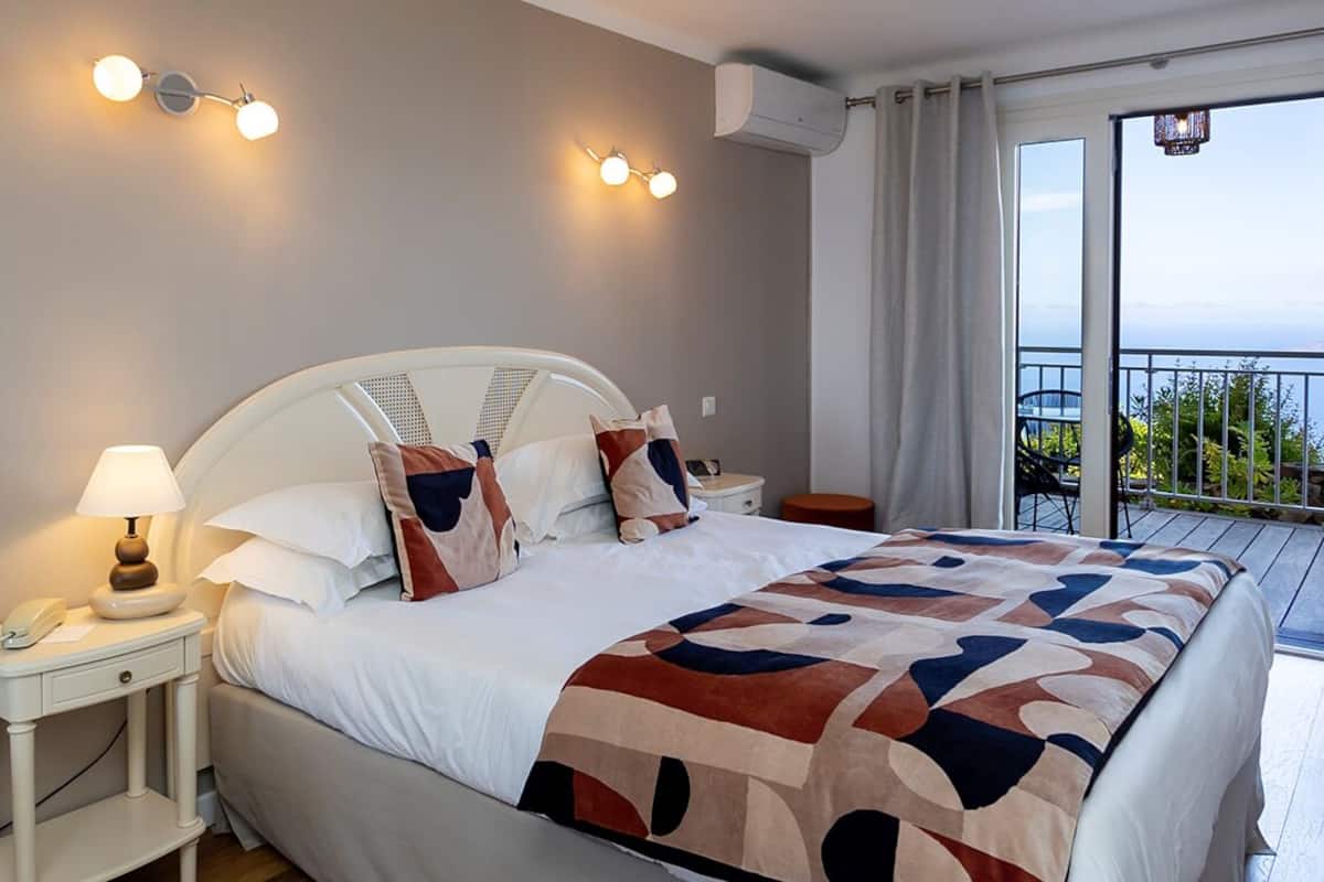A hotel room with a bed, bedside tables, a lamp, and a view of the outdoors.