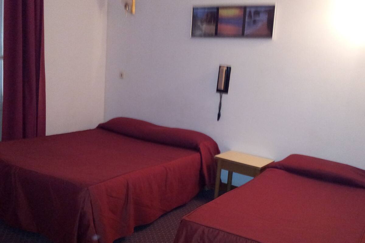 A room with two single beds, a small table, and a wall-mounted phone.