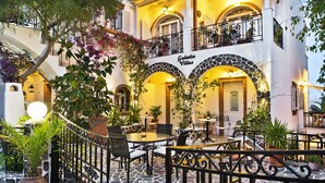A courtyard with outdoor seating, a stone floor, and a building with arches and balconies. - Galatia Villas (Santorini)