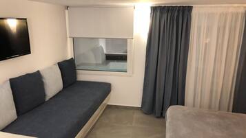 Ein modernes Zimmer mit grauem Sofa, kleinem Fenster und Blickfang sowie einem Vorhang.