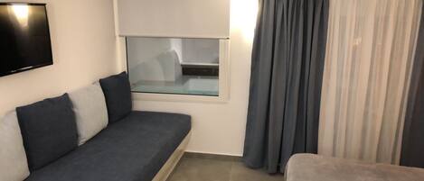 A modern room with a grey sofa, a small window with a view, and a curtain.