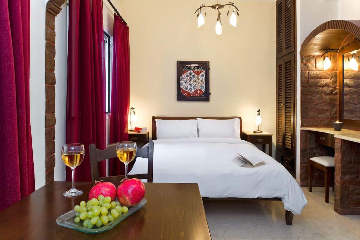 Een hotelkamer met een bed, een tafel met fruit en wijnglazen, een schilderij aan de muur en een stenen open haard.