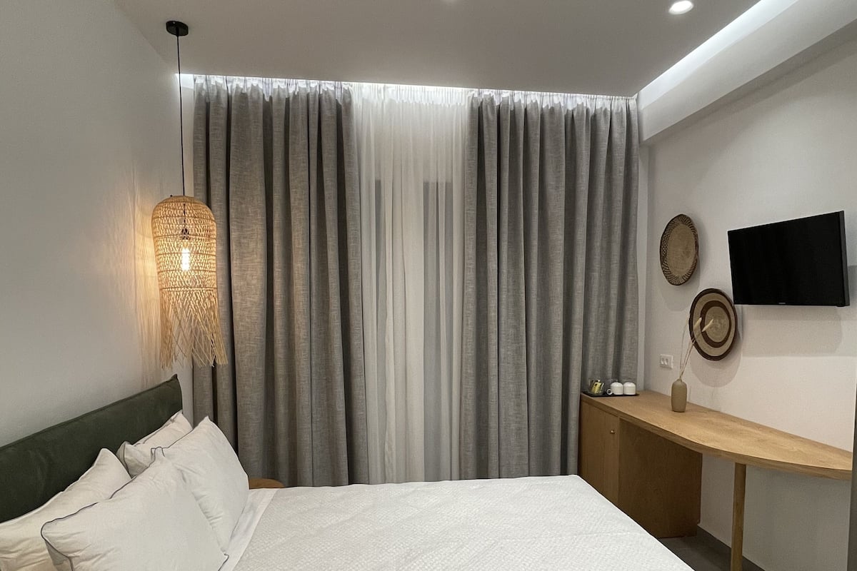 Een moderne slaapkamer met een groot bed, een nachtkastje, een televisie en een raam met gordijnen.
