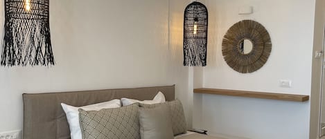 Un dormitorio moderno con una cama grande, dos lámparas colgantes, un espejo redondo y un estante de madera.