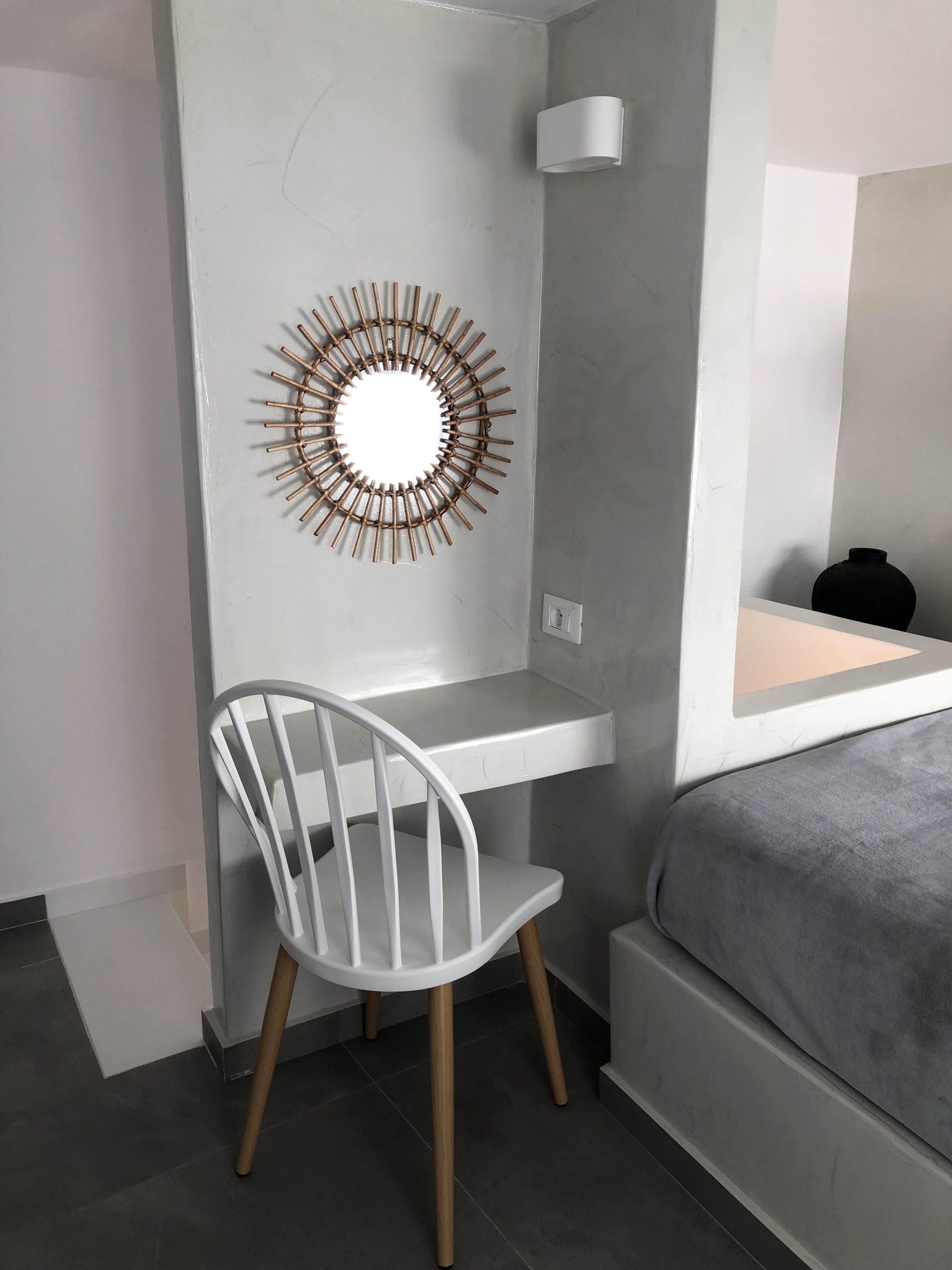 Ein modernes Schlafzimmer mit weißem Schreibtisch, weißem Stuhl, Nachttisch und einem großen Spiegel.