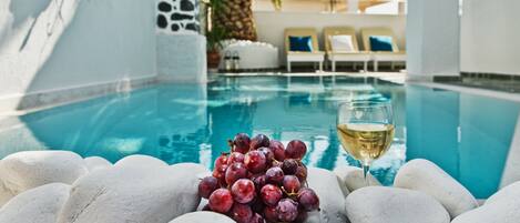 A pool area with white pebbles, a glass of white wine, and lounge chairs in the background.