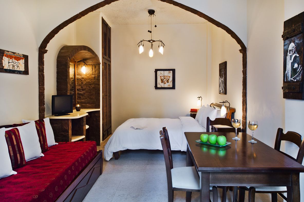 Een gezellige kamer met een bed, een rode bank, een eettafel met appels en wijnglazen, en een televisie op een bijzettafeltje.