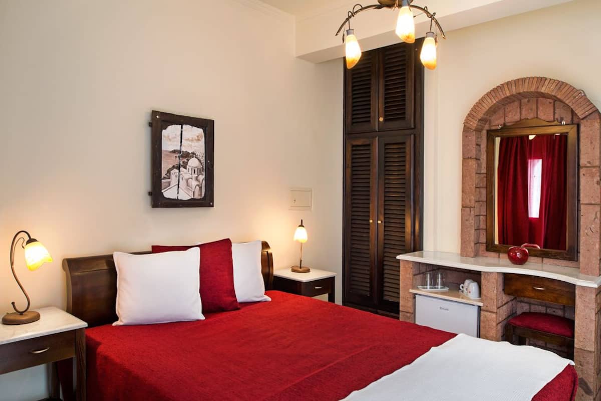 Een hotelkamer met een groot bed, twee nachtkastjes met lampen, een klein bureau, een spiegel en een rood gordijn, plus een foto aan de muur.