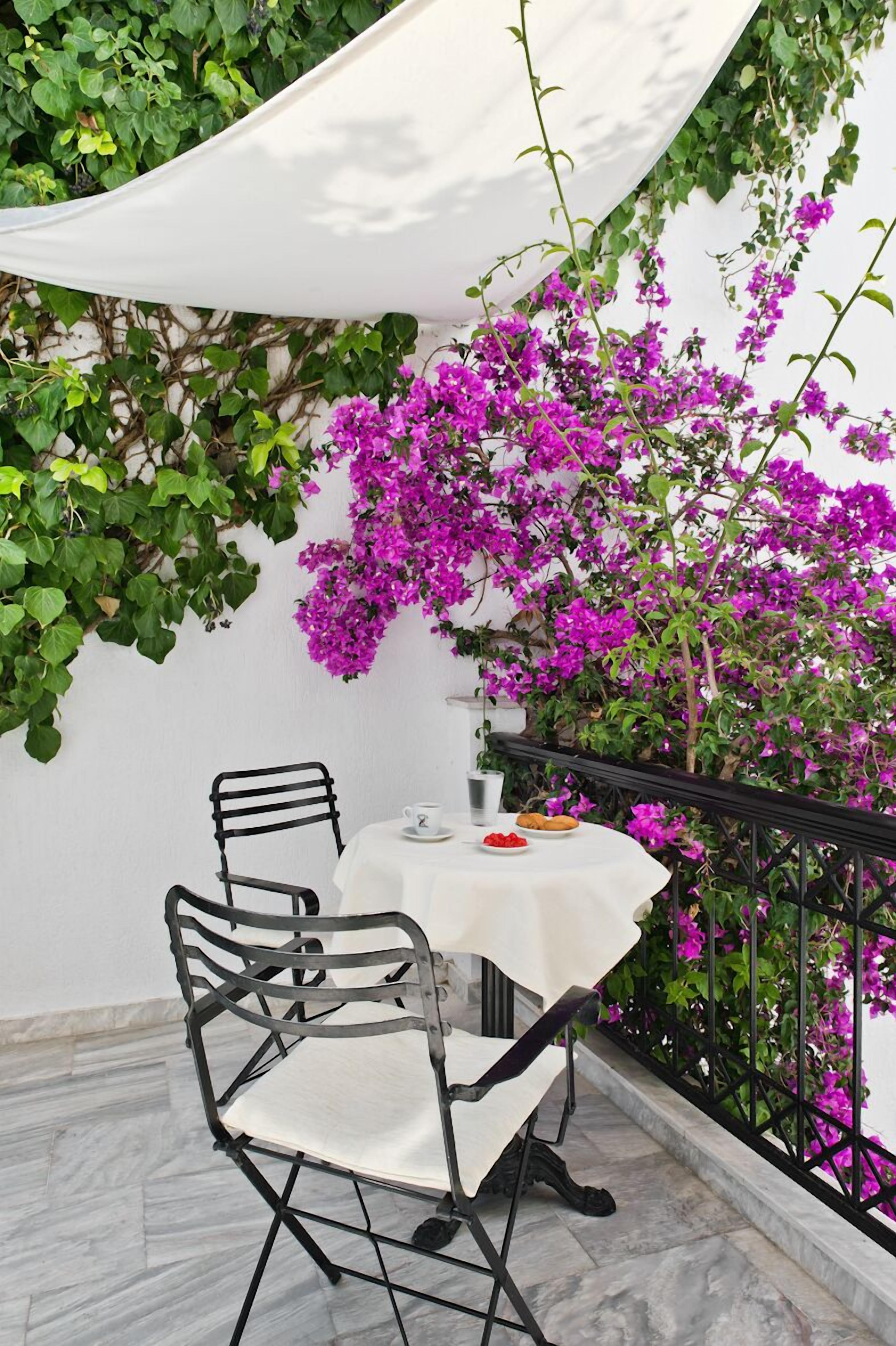 A small outdoor patio with a table and chairs, surrounded by a white wall and a black metal railing.