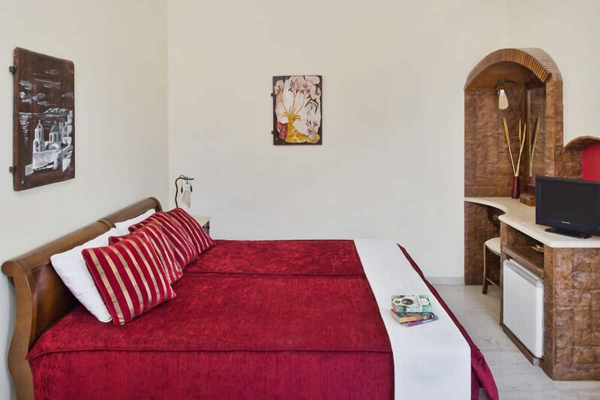 Een slaapkamer met een bed, een bureau, een televisie en kunstwerken aan de wanden.