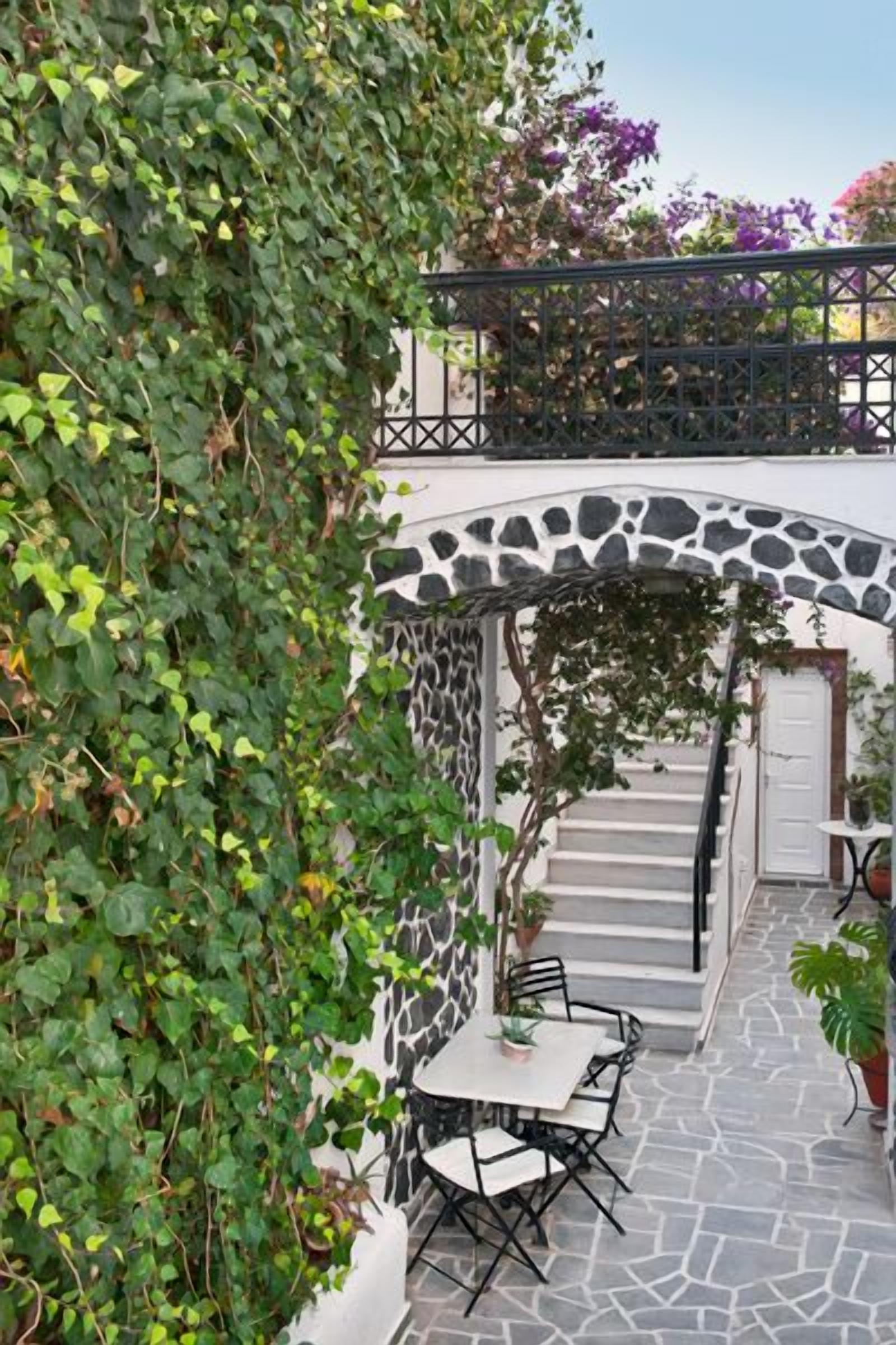 A stone staircase leading to a white door, surrounded by lush greenery and a stone floor.