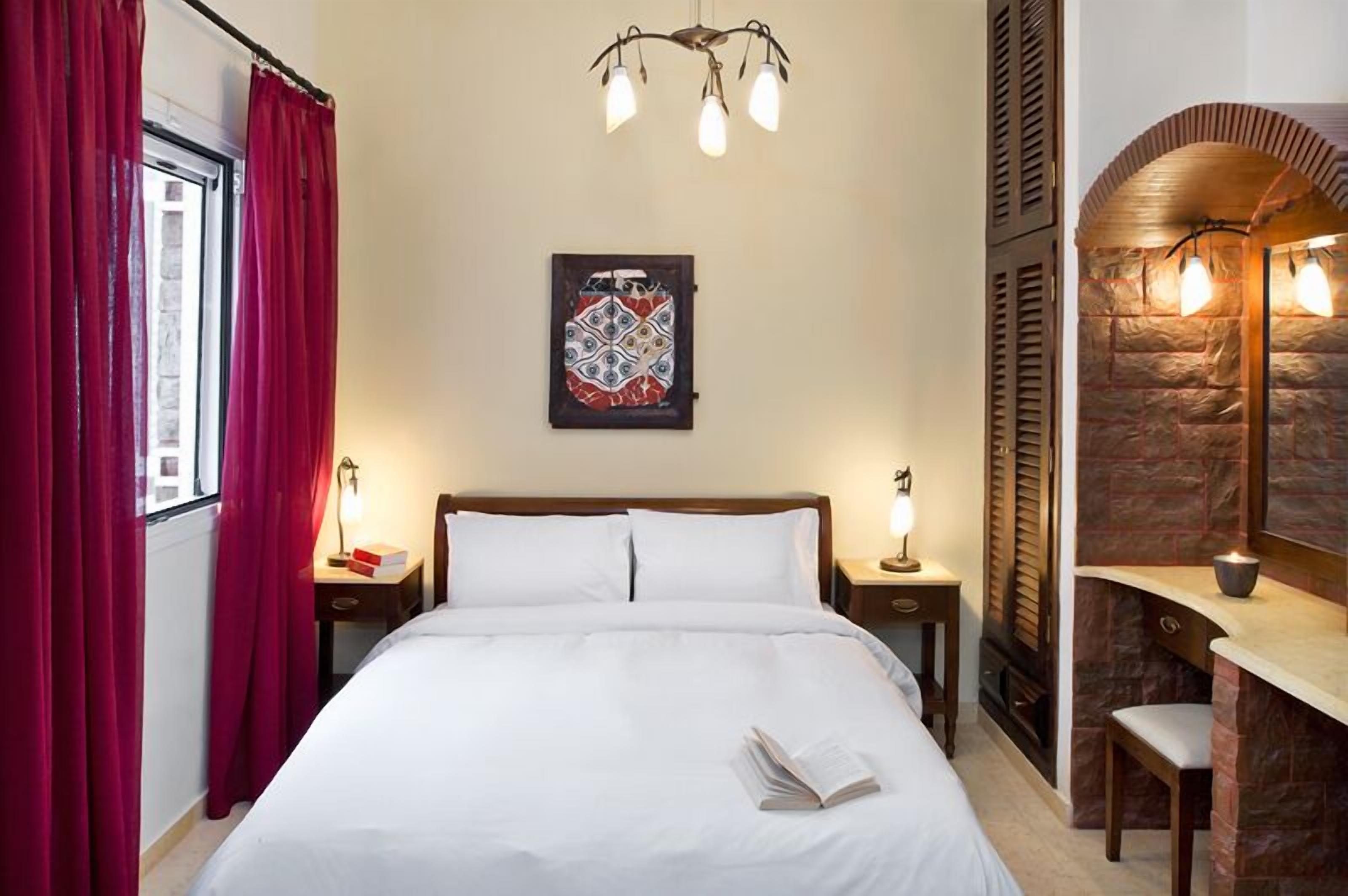 A neatly made bed with white linens, a bedside table with a lamp, a wall-mounted artwork, and a stone accent wall with a built-in shelf.
