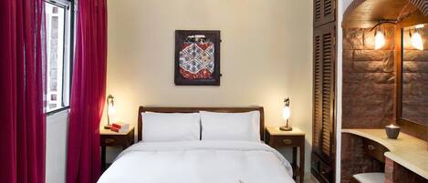 A neatly made bed with white linens, a bedside table with a lamp, a wall-mounted artwork, and a stone accent wall with a built-in shelf.