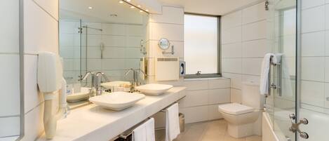 Un baño moderno con dos lavamanos, un inodoro y una ducha con mampara de vidrio.