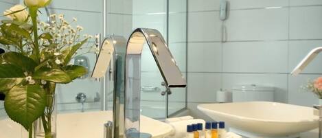 A modern bathroom with a glass shower enclosure, a white sink, and a vanity with toiletries.