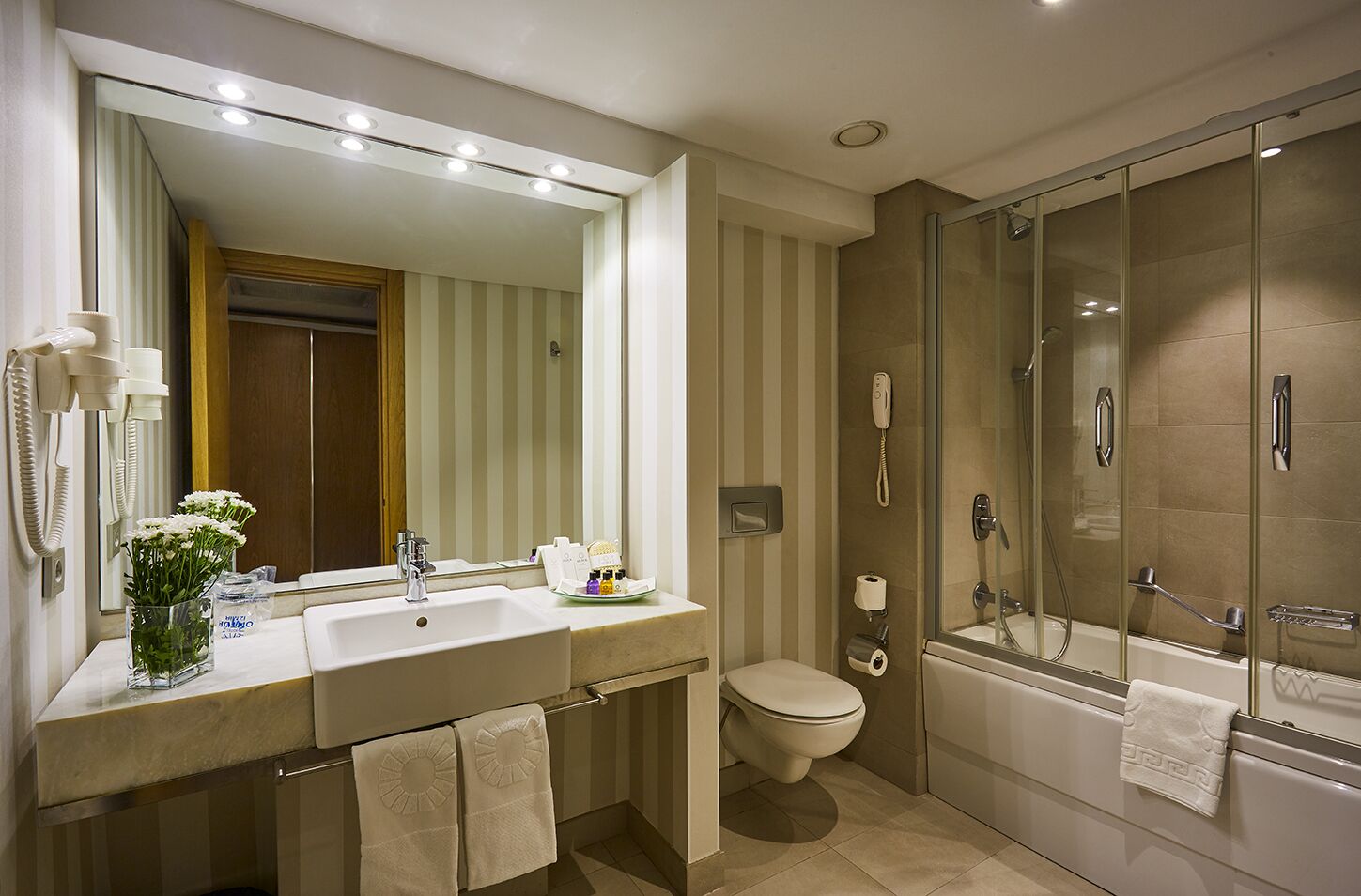 Un baño moderno con un espejo grande, dos lavamanos, un inodoro y una zona de ducha con mampara de vidrio.