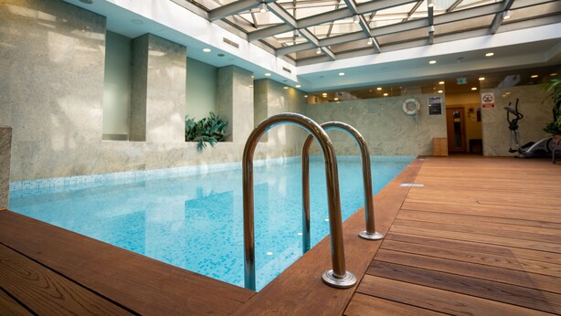 Una piscina interior con terraza de madera y techo de vidrio.