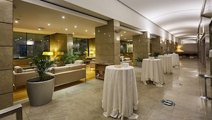 Un vestíbulo de hotel con zona de estar, mesas redondas y una planta grande en maceta.
