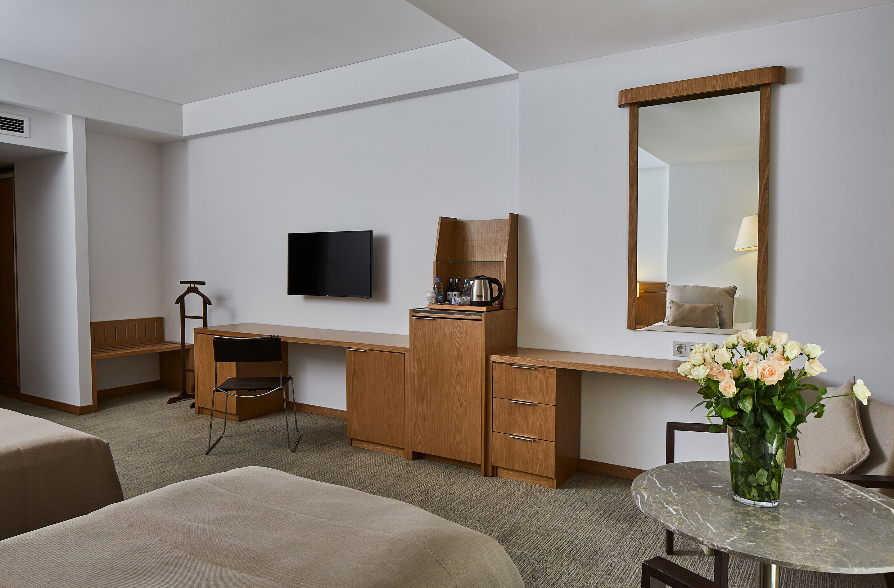 Ein Hotelzimmer mit einem Holztisch, einem Fernseher, einem Spiegel, einem kleinen Tisch mit Blumen und zwei Betten.