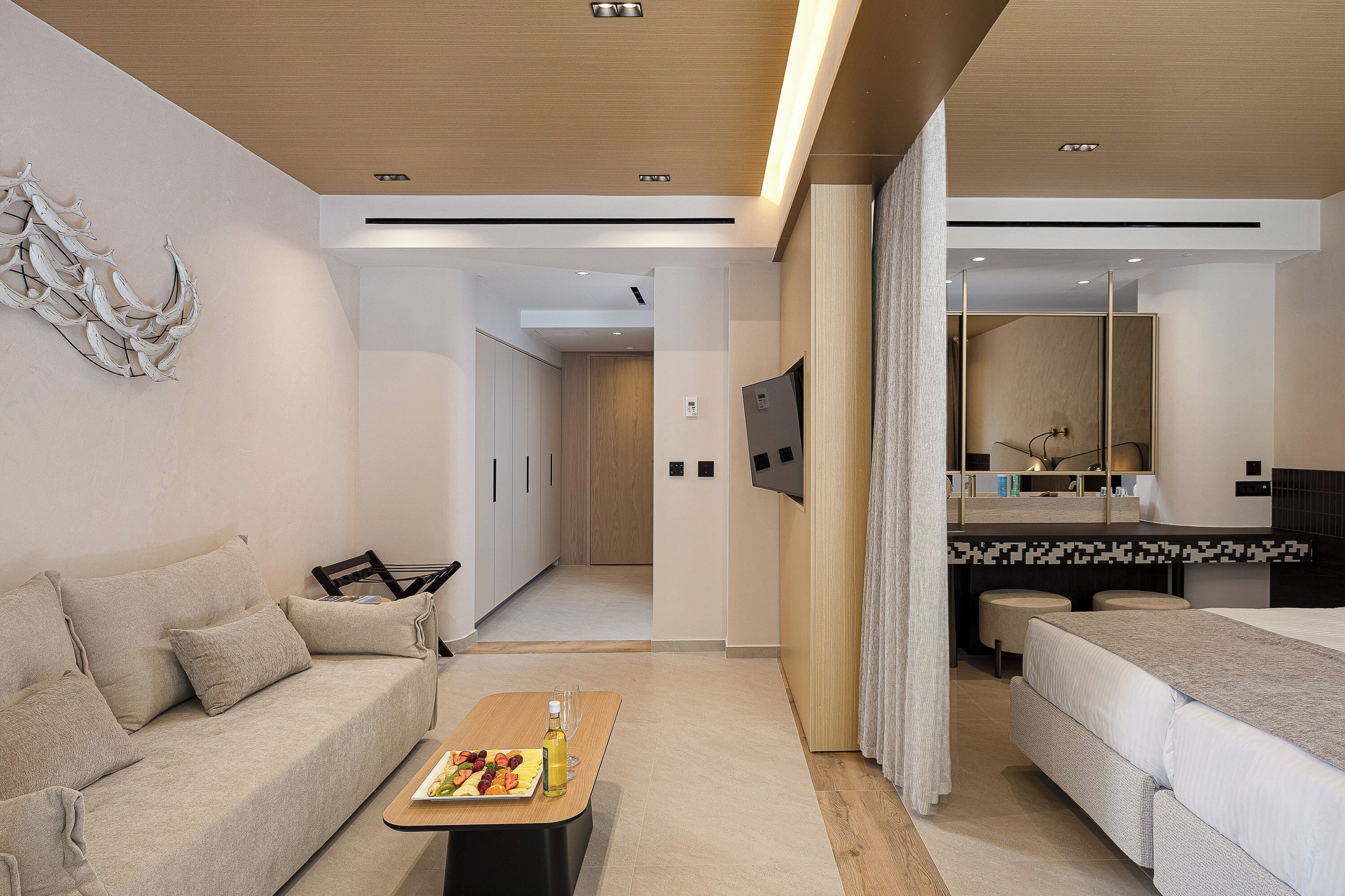 Een moderne hotelkamer met een bank, een eettafel met een bord eten, een bed, een televisie en een spiegel.