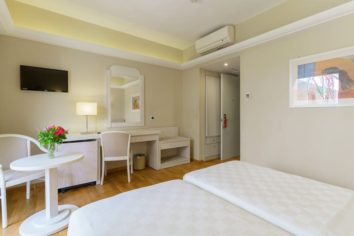 Una habitación de hotel con una cama, un escritorio, una silla, un televisor y un cuadro en la pared.