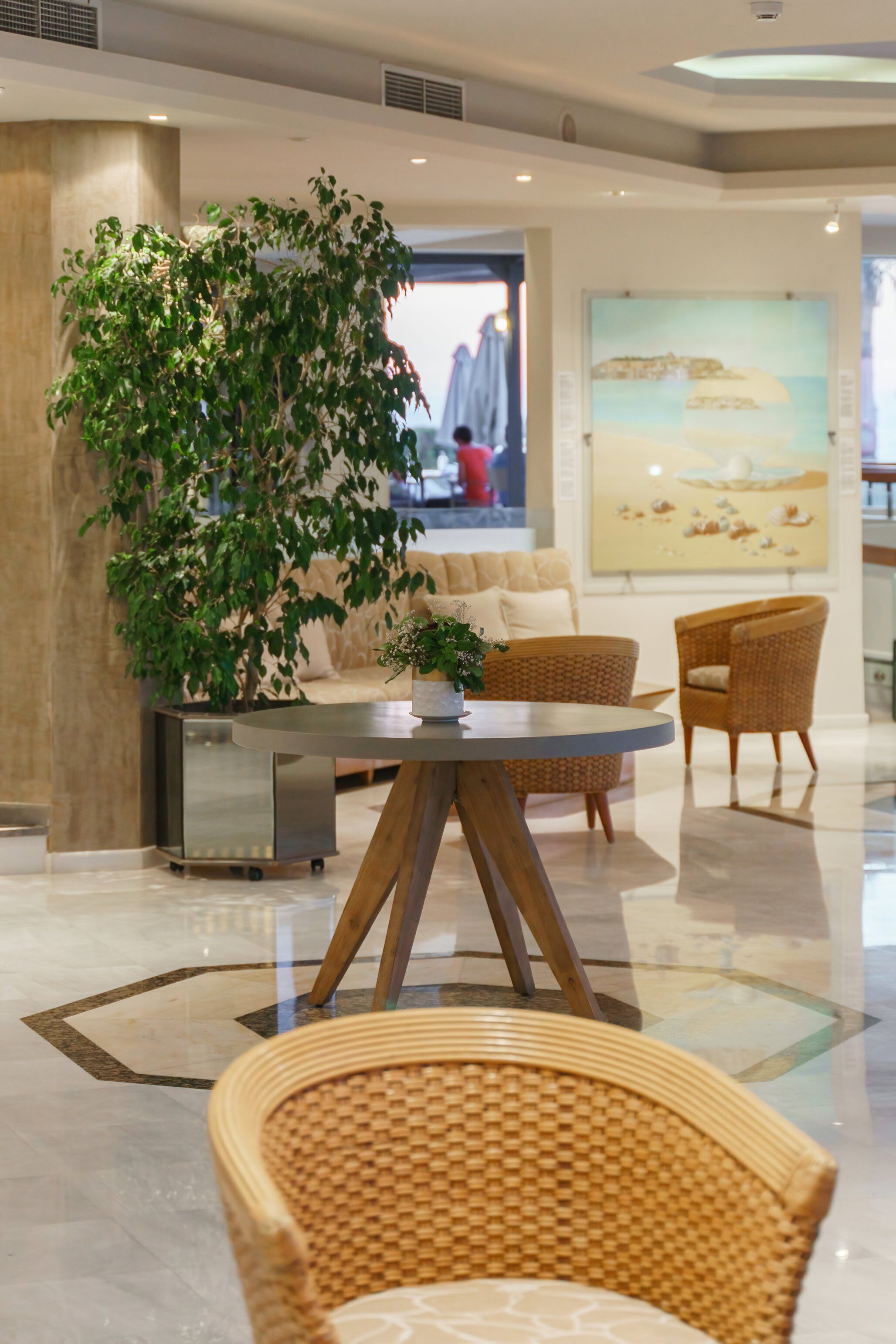 Un hall d’entrée avec une grande plante en pot, une table ronde entourée de chaises, un canapé et un grand tableau accroché au mur.