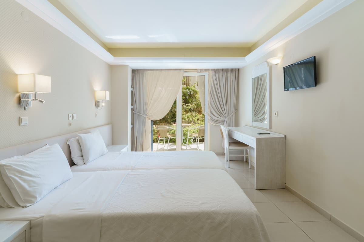 Habitación de hotel con dos camas, un escritorio, un televisor y un balcón con cortinas.