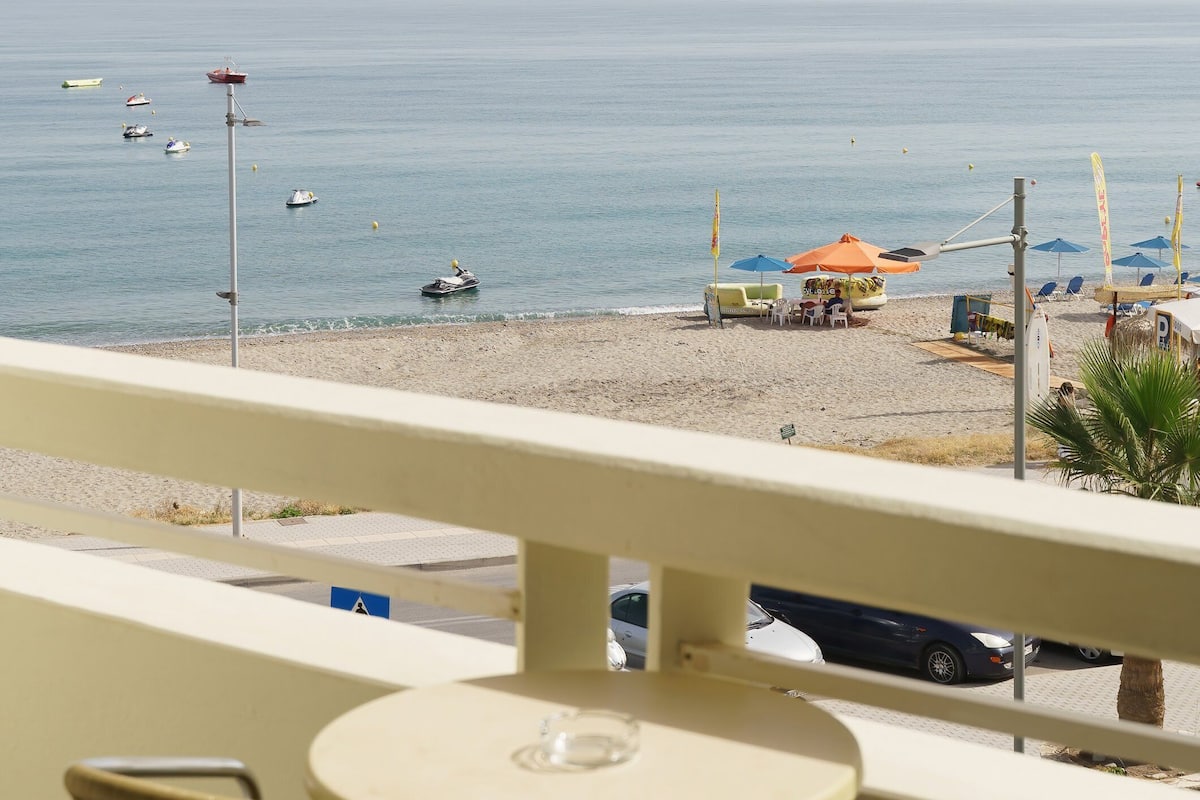 Un balcón con vista a la playa, una mesa y sillas.