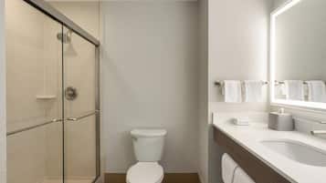 Un baño moderno con cabina de ducha de vidrio, inodoro blanco y tocador con espejo y toallero.