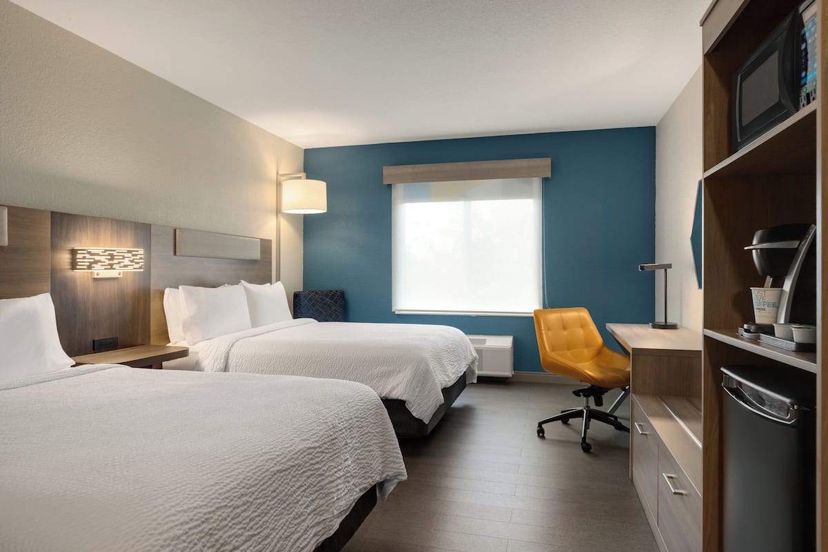 Une chambre d’hôtel avec deux lits, un bureau, une chaise, un four à micro-ondes et un réfrigérateur.