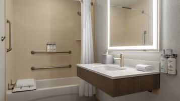 Un baño moderno con bañera, lavabo y espejo. Hay barras de apoyo y un perchero para toallas.