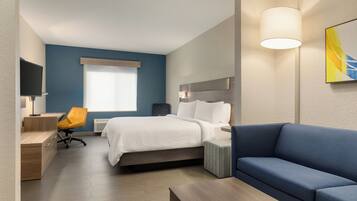 A modern hotel room with a bed, a blue sofa, a desk with a chair, and a TV.