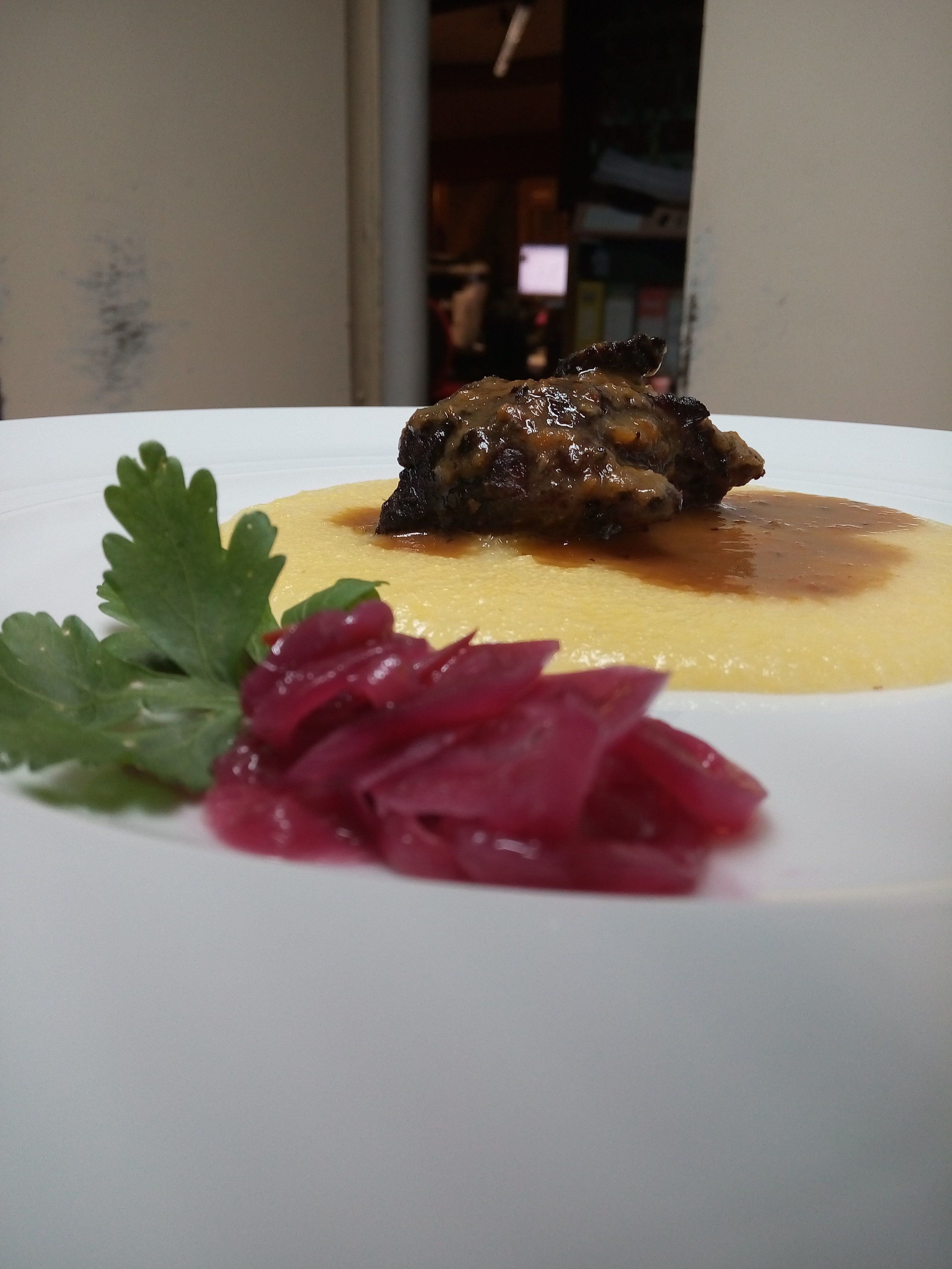 A plate with a piece of meat, a yellow puree, and red cabbage garnish.