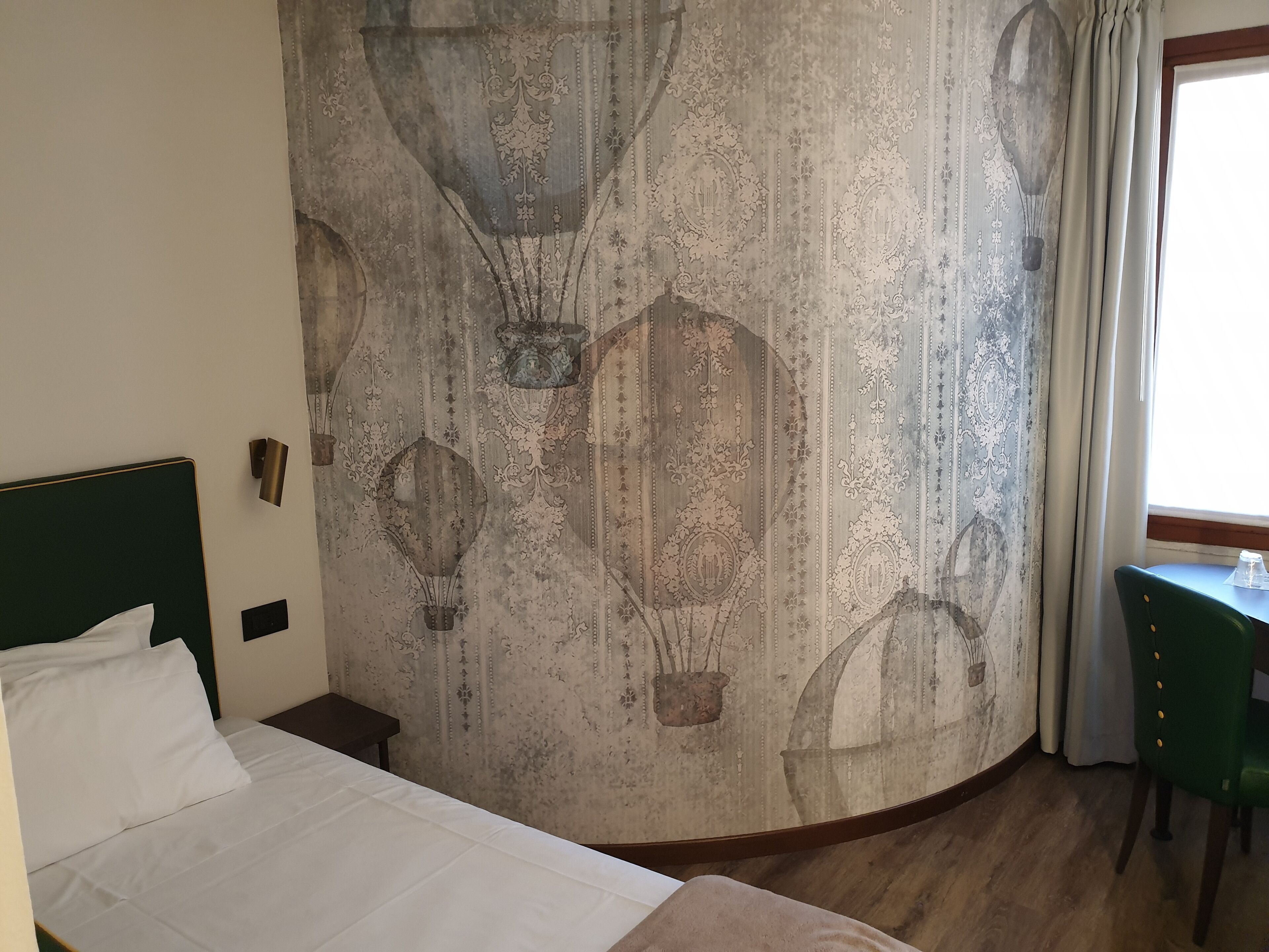 Una habitación de hotel con cama, escritorio y pared decorada con un diseño de papel tapiz antiguo.