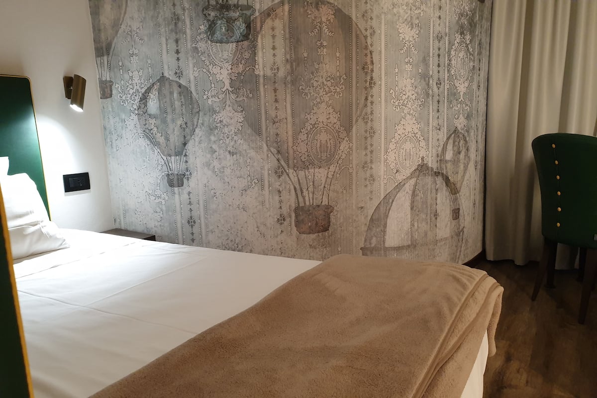 A hotel room with a bed, a green chair, and a wall with a patterned design.