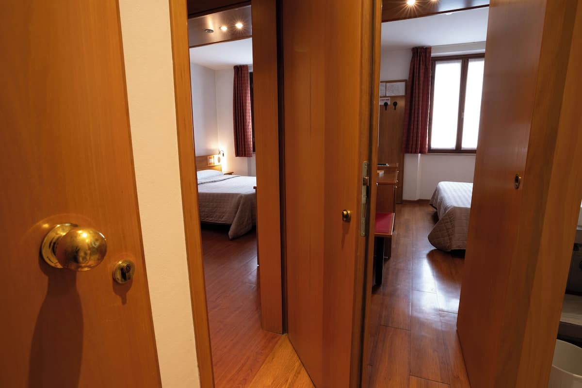 A hotel room with a wooden floor, two beds, a desk, and a window with curtains.